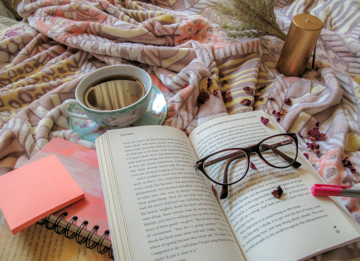 Open book with glasses, teacup, and notebook on a blanket.