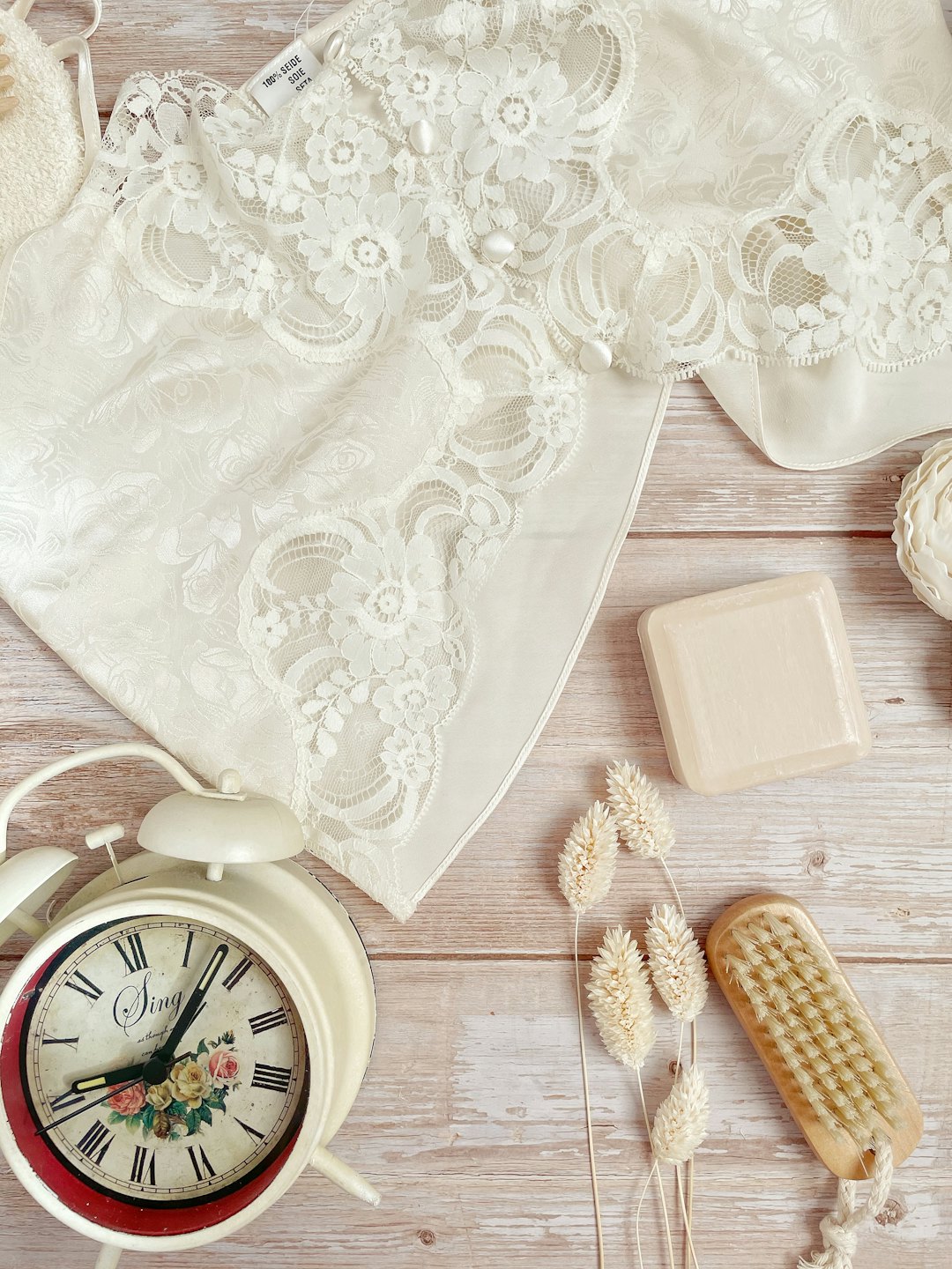 Lace garment, alarm clock, soap, and brush on wooden surface.