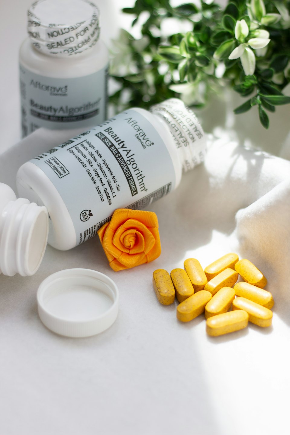 Two supplement bottles and yellow pills with a fabric rose.